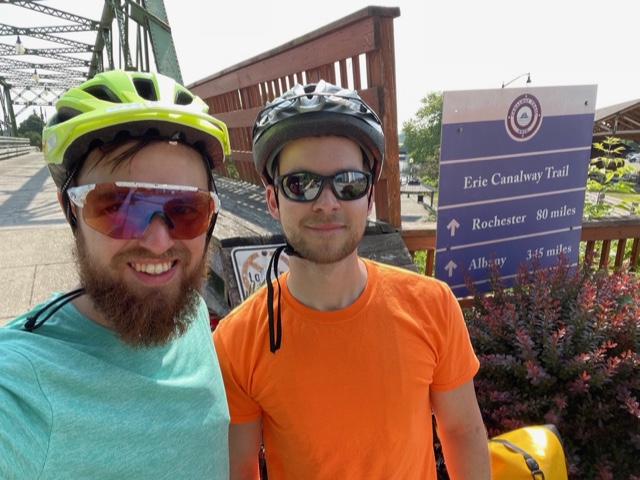 Myself and a friend standing in front of a bridge with a sign for the Erie Canal saying that Rochester is 80 mies away.